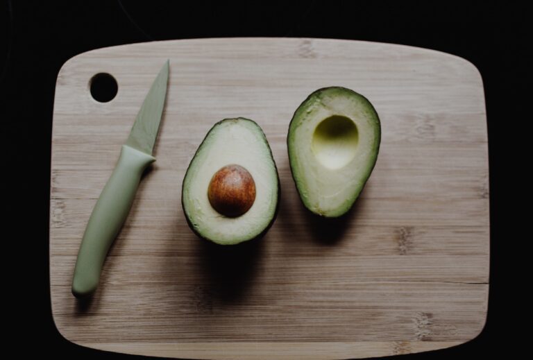 An avocado sliced in half on a wooden cutting board.