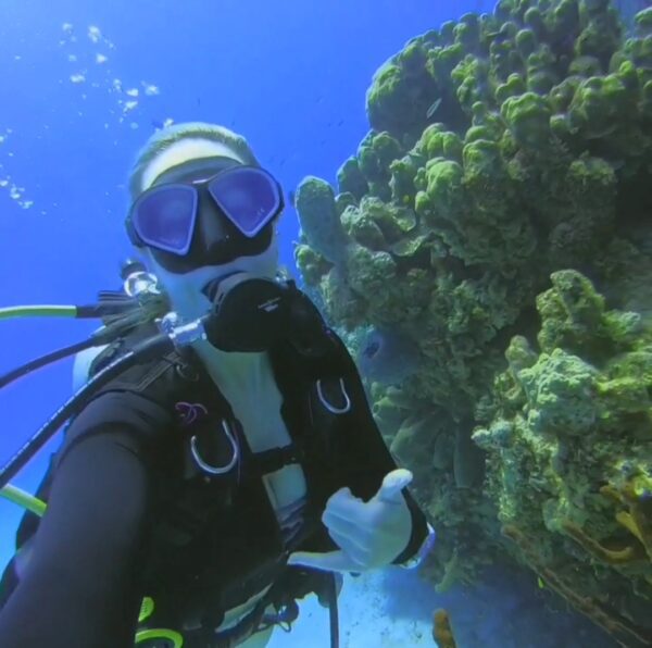 Underwater picture of Christina Kathleen SCUBA diving next to healthy coral in Grand Cayman.